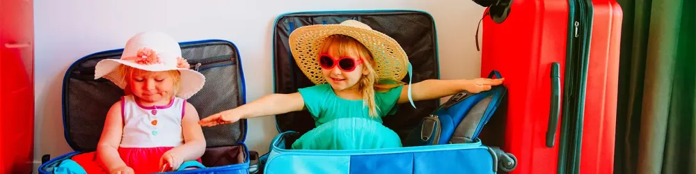 Children playing inside suitcases next to packed luggage